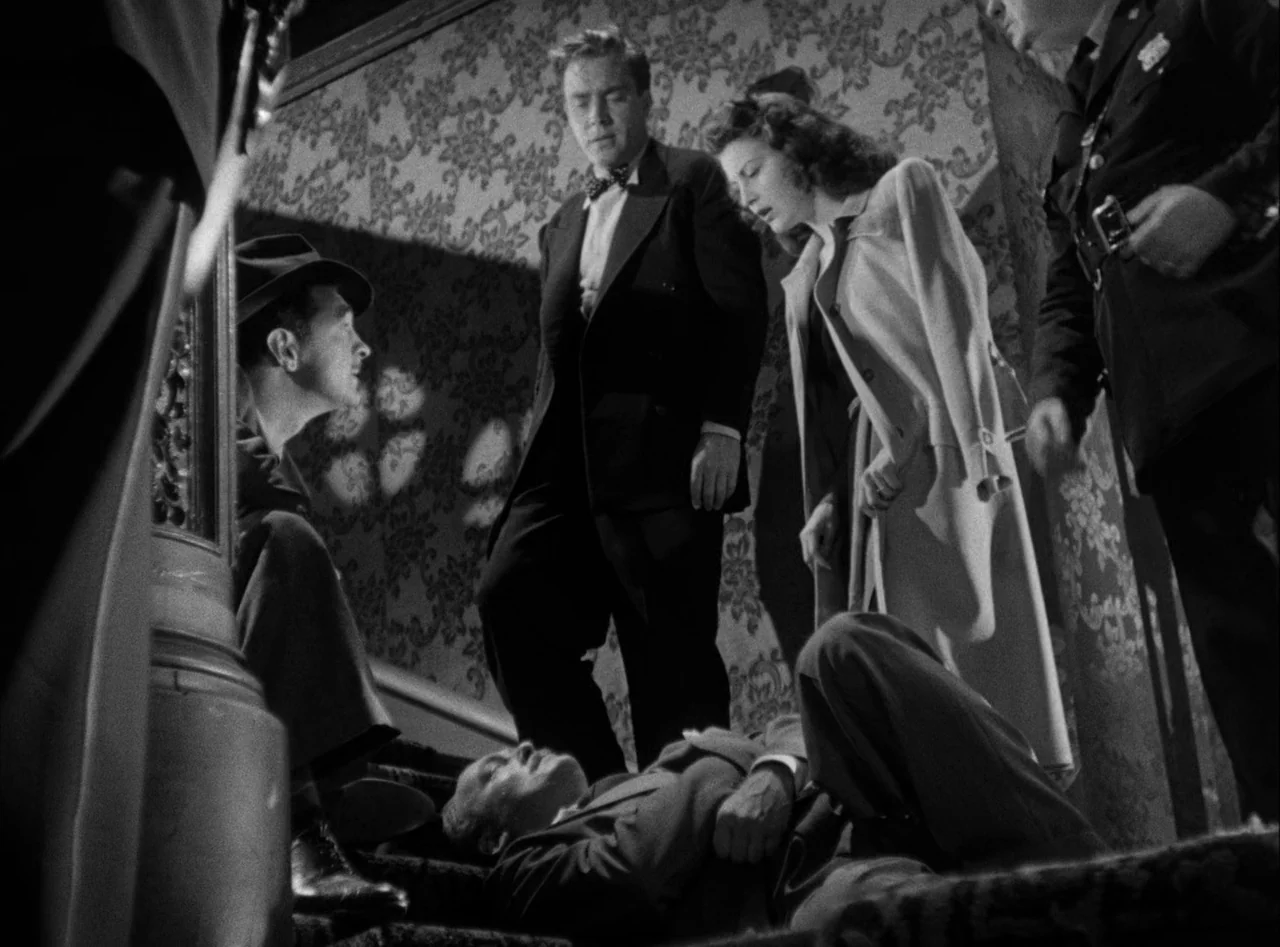 The Killers (1946) movie still: fullbody — A dimly lit indoor staircase features ornate damask wallpaper and patterned carpeted steps. Four people…