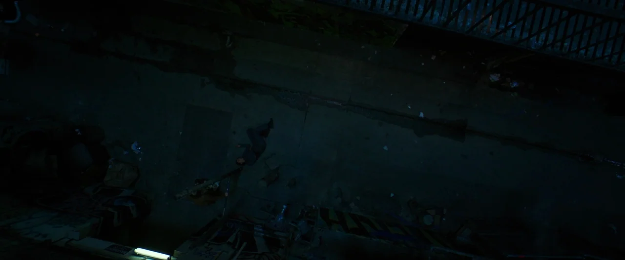 Hotel Artemis (2018) movie still: wide — A dark, narrow urban passageway shows graffiti on the brick walls and wet pavement. One person lies…