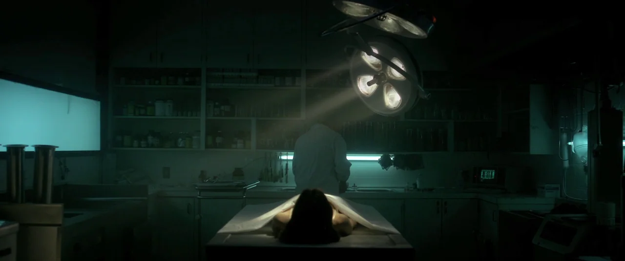 The Void (2016) movie still: wide — A dark, clinical morgue room features rows of storage cabinets and stainless steel surfaces. A person in a white…