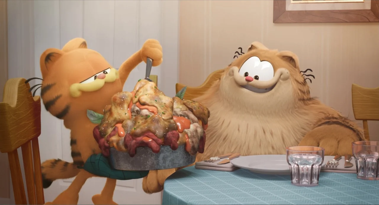 The Garfield Movie (2024) movie still: medium — A domestic dining room with simple wooden chairs and a blue patterned tablecloth. Two orange cartoon…