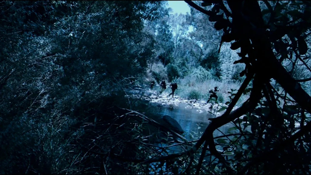 Che Part 2 (Guerrilla) (2008) movie still: wide — A group of soldiers move through a creek surrounded by dense, dark vegetation. The dark…