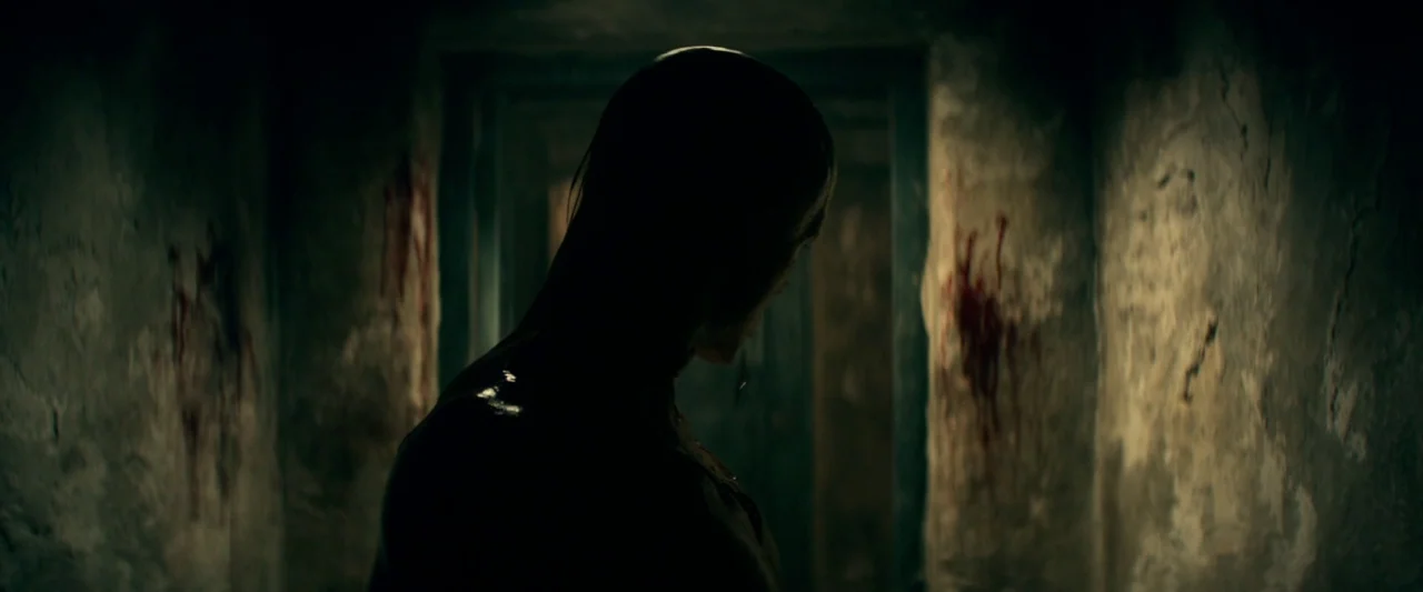 Overlord (2018) movie still: medium — A dark, narrow stone hallway has vertical smears of dried blood on the walls. A lone, shirtless man stands…