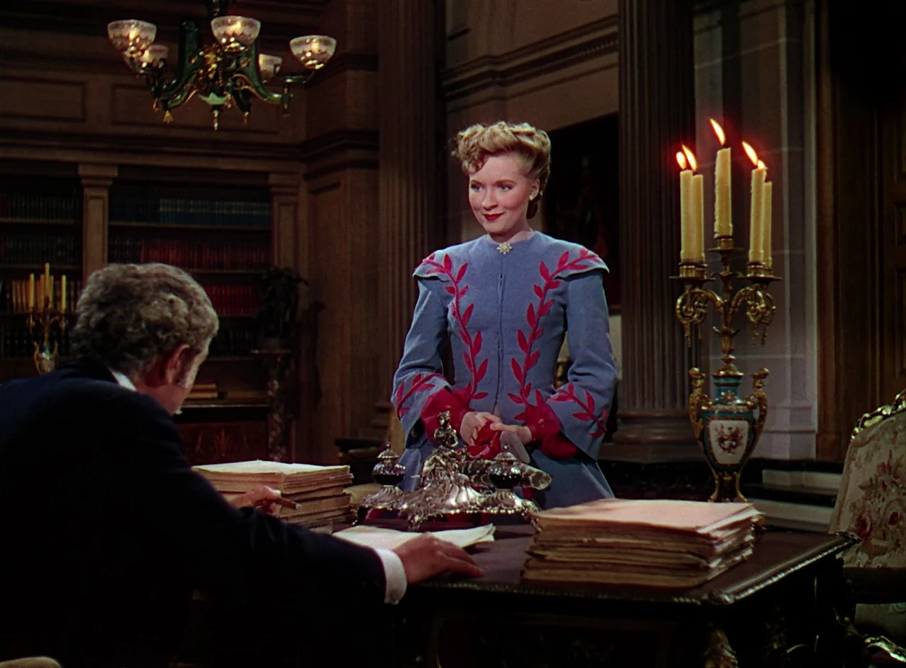 Phantom of the Opera (1943) movie still: medium — An ornate wood-paneled room features bookshelves, a large desk, and a candelabra. A woman in an…