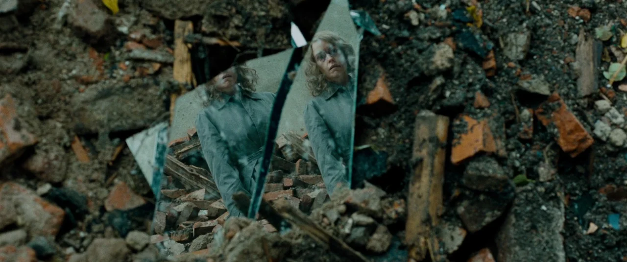Phoenix (2014) movie still: closeup — A woman's reflection appears in a sharp shard of glass embedded in rubble. The surrounding environment…