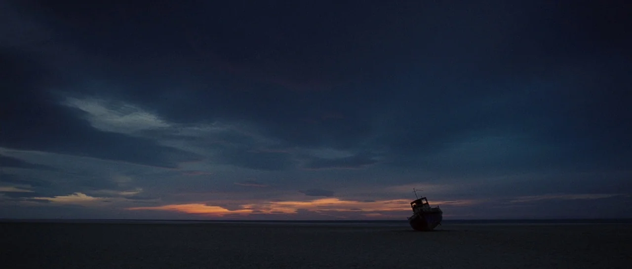 Never Let Me Go (2010) movie still: establishing — A dark, expansive beach stretches out under a twilight sky with low-hanging clouds. An abandoned…