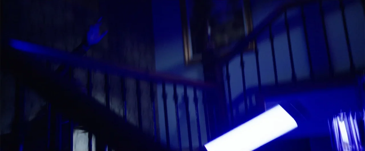 Lights Out (2016) movie still: medium — A dark residential staircase is illuminated by harsh blue light from below. A single subject ascends the…