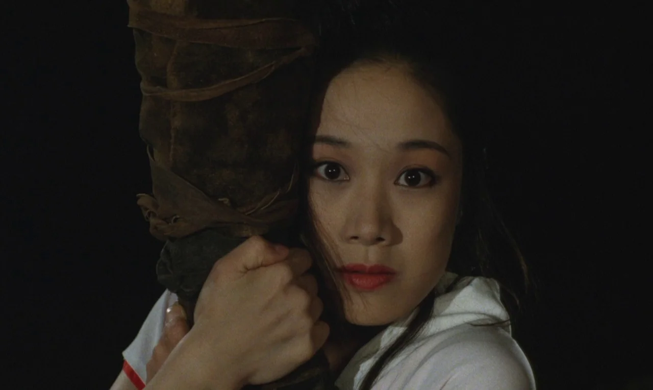 Yumeji (1991) movie still: closeup — The background is completely black, isolating the subject in a void-like space. A young woman with dark hair…
