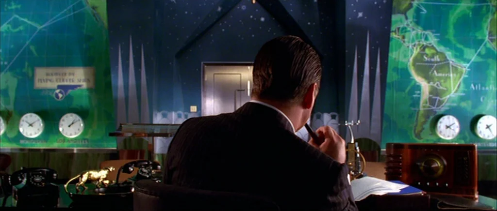 The Aviator (2004) movie still: medium — A dark office features green wall maps and multiple clocks indicating different time zones. A man in a…
