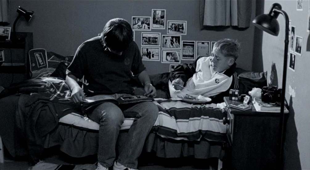 Somers Town (2008) movie still: medium — A teenage bedroom features walls decorated with small black and white framed photographs. Two young men sit…