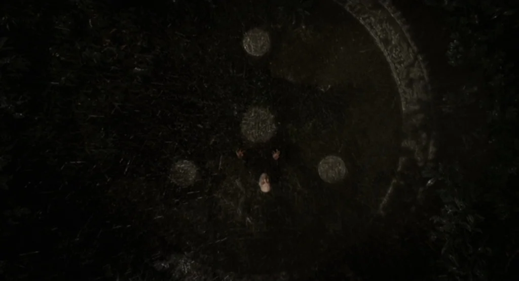The Fountain (2006) movie still: wide — An ancient stone circle with circular carvings on the ground sits in dark woods. An elderly man stands in…