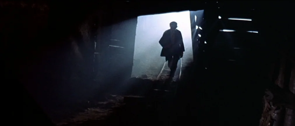 Fistful Of Dollars (1964) movie still: wide — A dark, rough-hewn mine tunnel features wooden beams and narrow metal tracks on the ground. A single…
