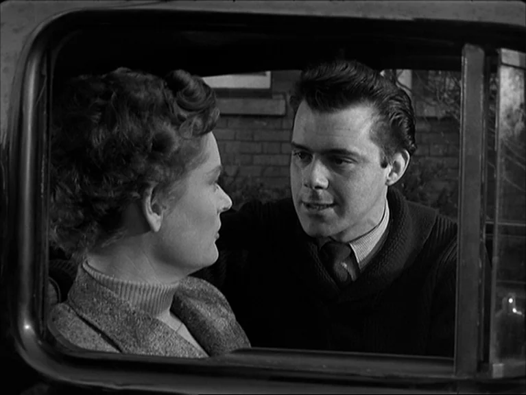 The Sleeping Tiger (1954) movie still: medium — The interior of a vintage car at night viewed through the side window. A man in a dark knit sweater…