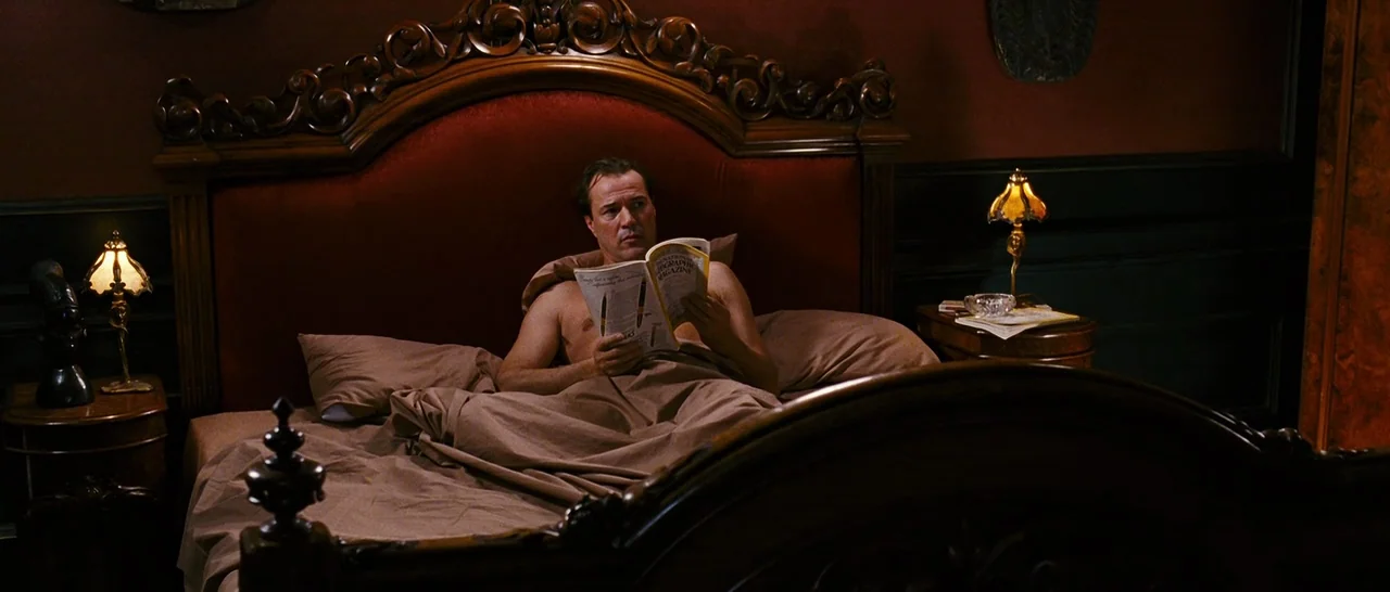 Black Book (2006) movie still: medium — A dark, wood-paneled bedroom features a large, ornate mahogany bed with a velvet headboard. A middle-aged…
