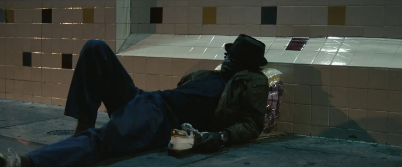 Into the Wild (2007) movie still: fullbody — A man rests on a concrete sidewalk against a patterned ceramic tiled wall. He is reclined on the ground…