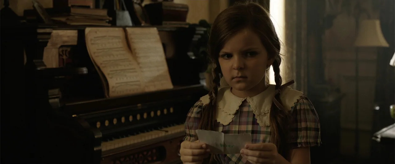 Annabelle: Creation (2017) movie still: medium — A dark, dimly lit room contains an old wooden piano in the background. A young girl in a plaid…