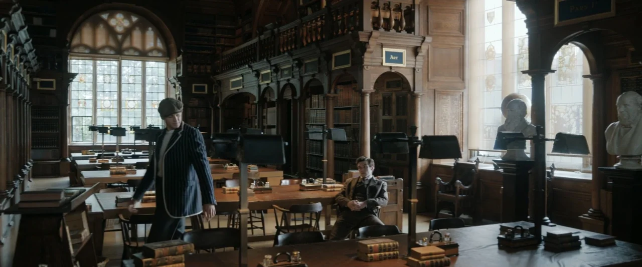 Young Sherlock Holmes (1985) movie still: medium — A historic wooden library features ornate shelving units, arched windows, and antique study…