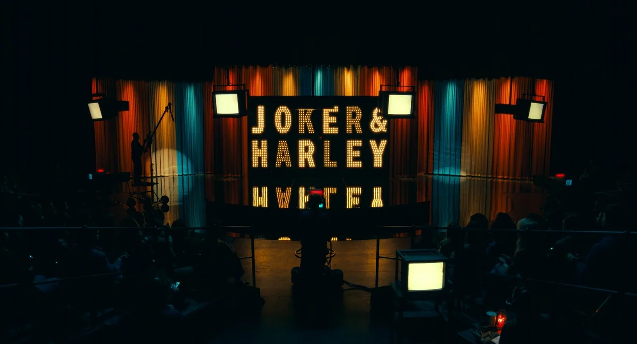 Joker: Folie à Deux (2024) movie still: wide — A television soundstage features a large marquee sign reading Joker and Harley. Colorful vertical…