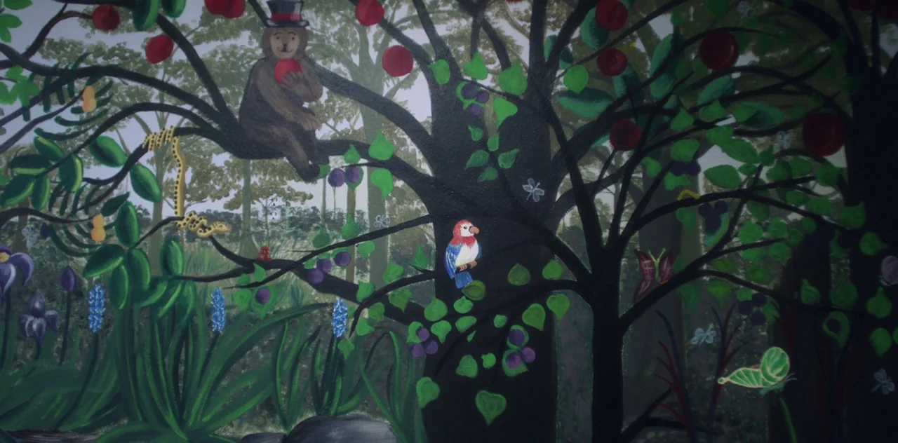 Darlin’ (2019) movie still: wide — A flat, painted mural depicts a dense stylized woodland setting with varied flora and fauna. A bear in a top hat…