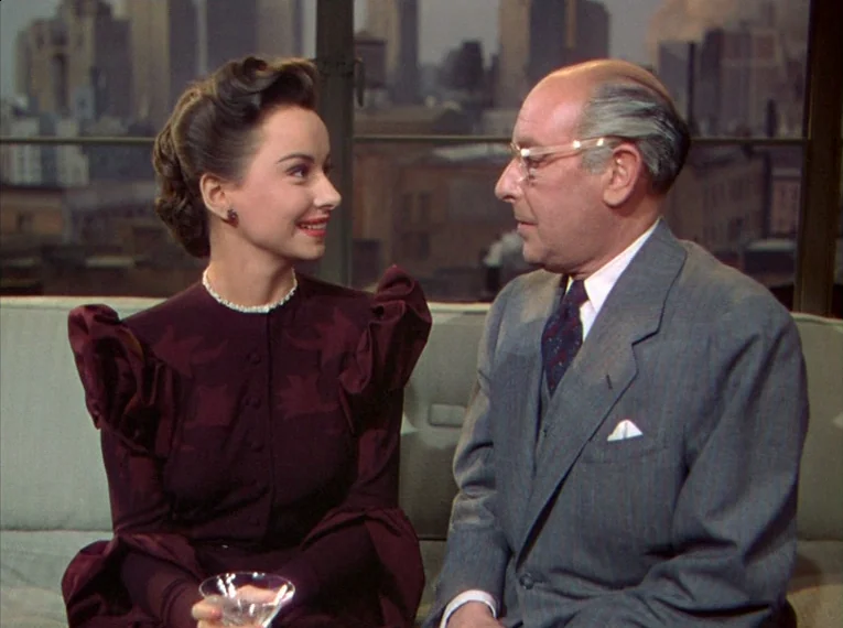 Rope (1948) movie still: medium — A high-rise interior space with a window overlooking an out-of-focus urban cityscape. A young woman and an elderly…