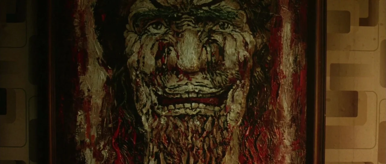 Oldboy (2003) movie still: closeup — A dark framed painting displays a textured, abstract human face with a wide grin. The painting is mounted on a…