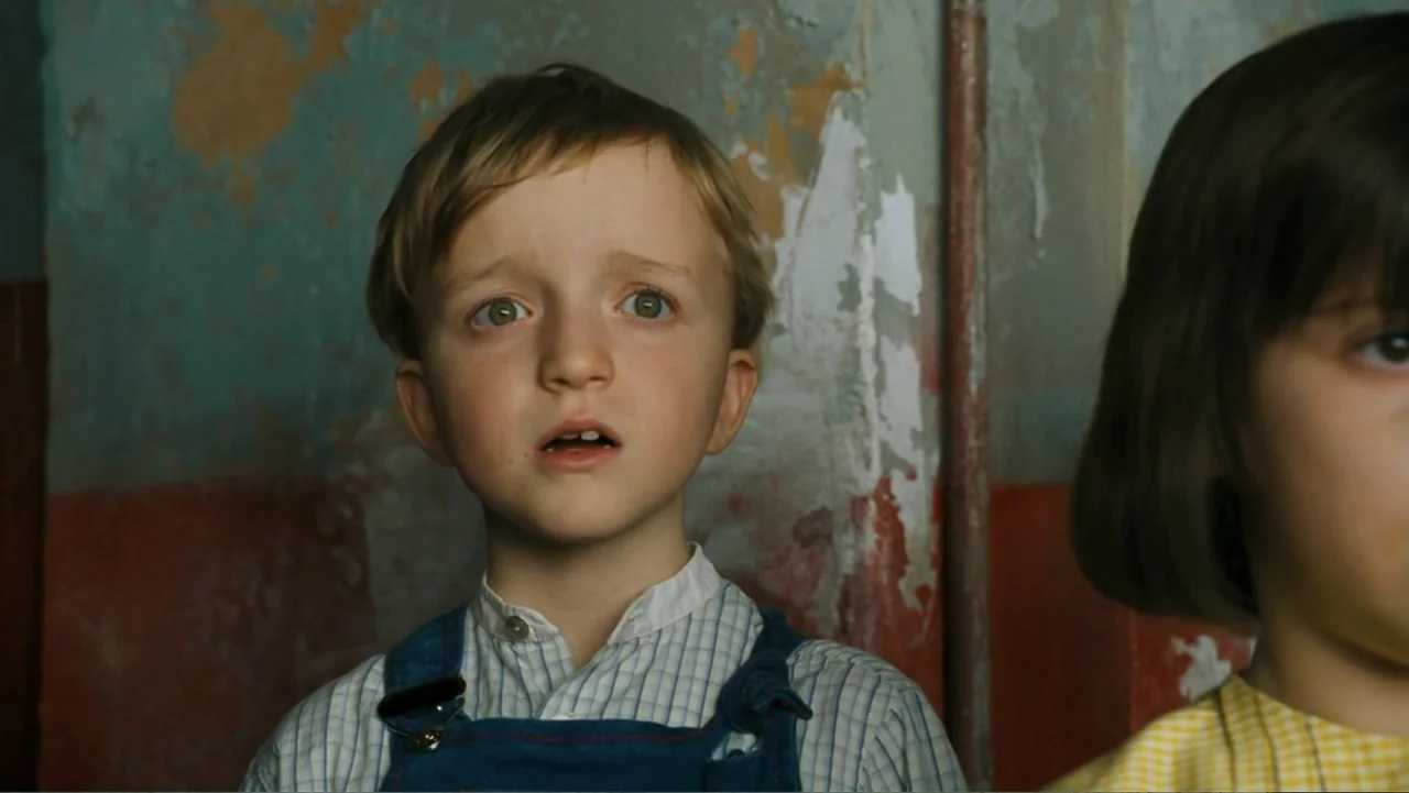 Nanny McPhee and the Big Bang (2010) movie still: closeup — A room with weathered walls showing peeling paint and layered textures. A young boy in…