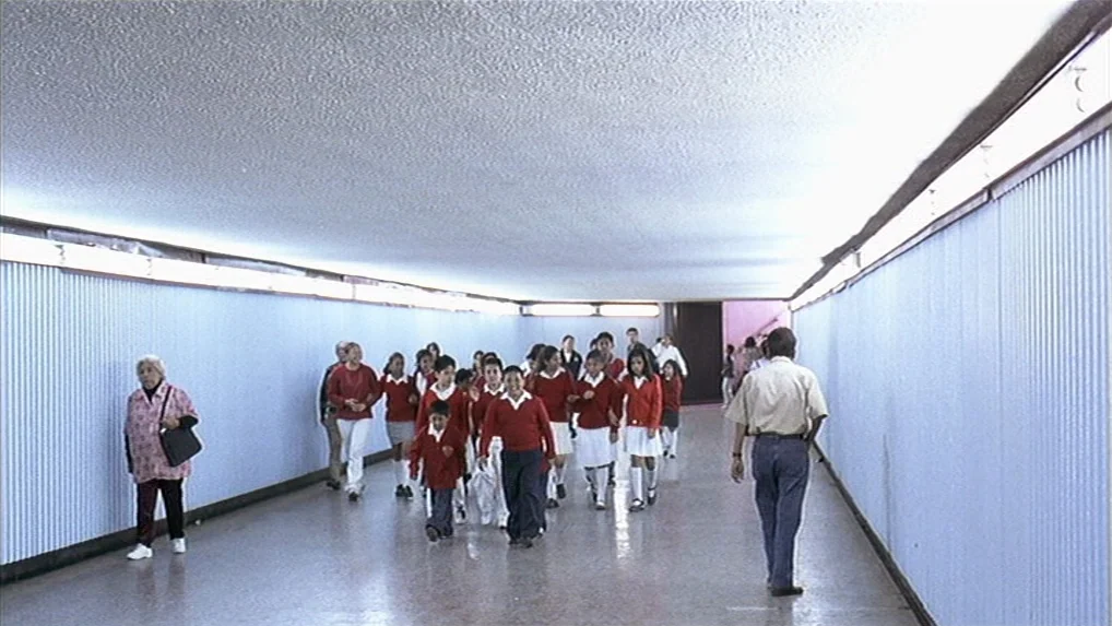 Battle In Heaven (2005) movie still: wide — A long, institutional pedestrian underpass features light blue corrugated metal walls and white…
