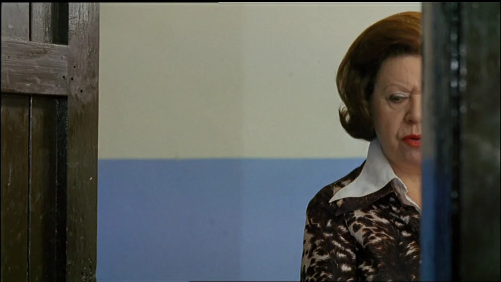 Chinese Roulette (1976) movie still: closeup — A woman stands in a corridor with light blue and off-white painted walls. She looks toward the side…