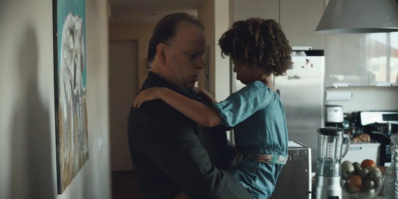 Equal Standard (2021) movie still: medium — A modern kitchen contains stainless steel appliances and a colorful framed painting on the wall. An…