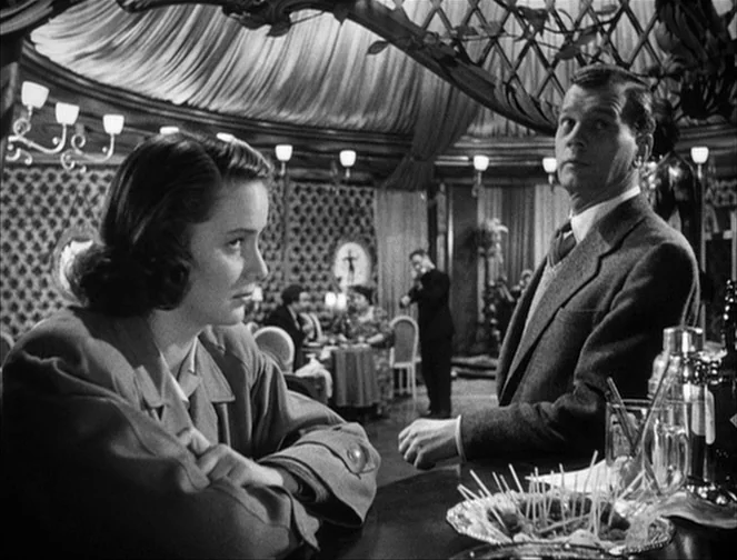 The Third Man (1949) movie still: medium — A dimly lit restaurant interior features draped ceiling fabric and patterned wallpaper backdrop. A man…