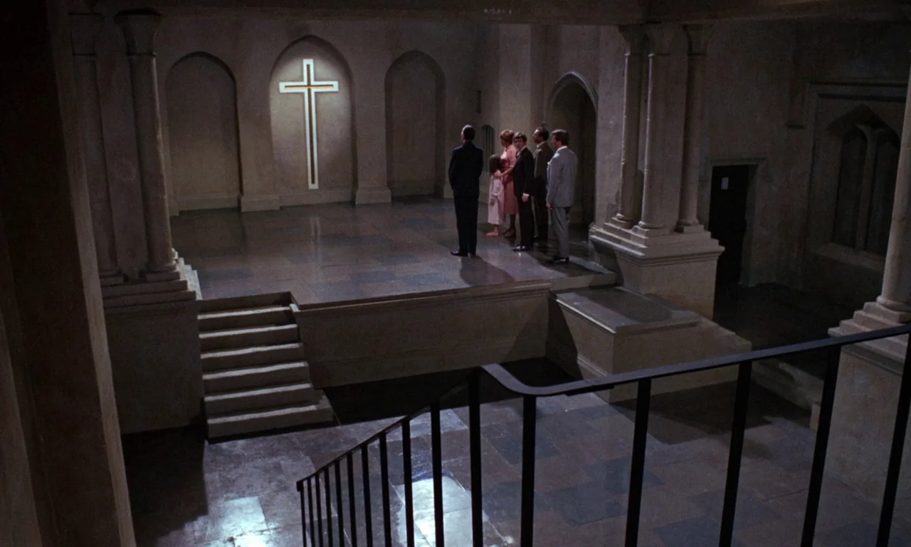 The Devil Rides Out (1968) movie still: wide — A stone subterranean room with arched alcoves and a central raised platform. Six people stand in a…