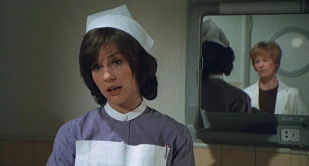 Blood From The Mummy’s Tomb (1971) movie still: medium — A sterile administrative area featuring beige tiled walls and a wall-mounted mirror. A…