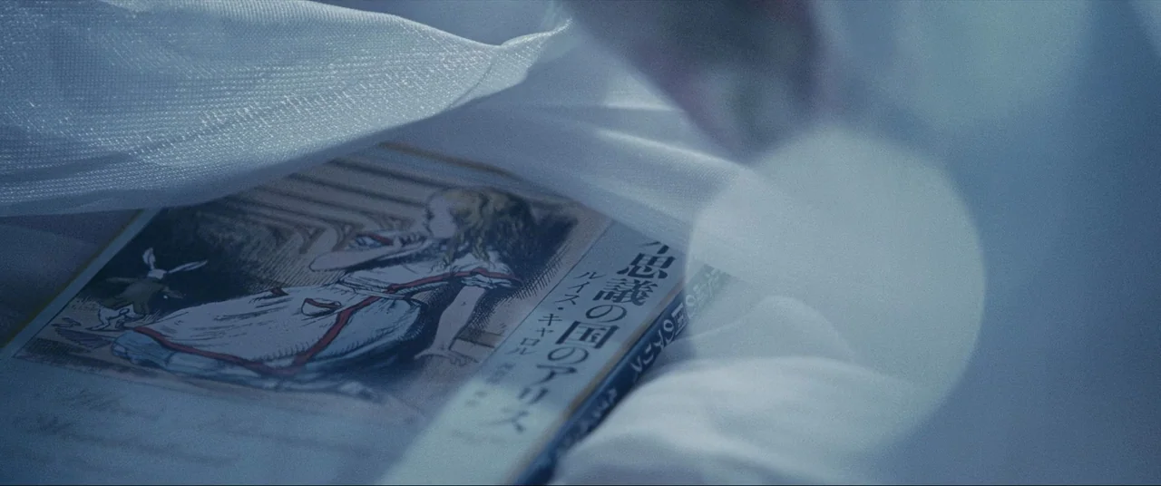The World of Kanako (2014) movie still: closeup — A Japanese edition of Alice in Wonderland rests on white, sheer fabric. The book is partially…