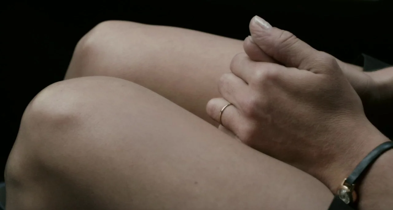 Bastards (2013) movie still: closeup — The interior of a vehicle shows a person sitting with knees bent. Hands rest clasped upon the lap with a…