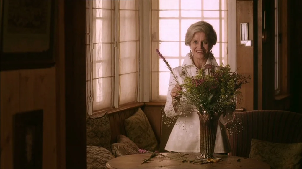 Away From Her (2006) movie still: medium — A light-filled room with wood paneling and a large window features a corner booth. An older woman smiles…