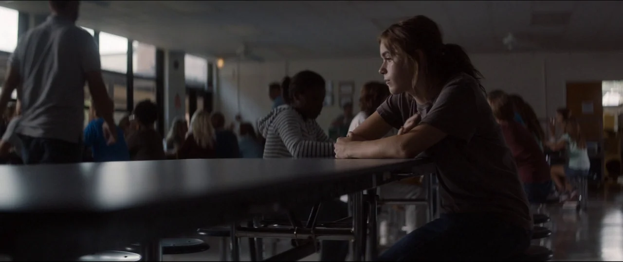 One & Two (2015) movie still: medium — A dimly lit school cafeteria features long metallic tables and rows of seated students. A young girl sits…