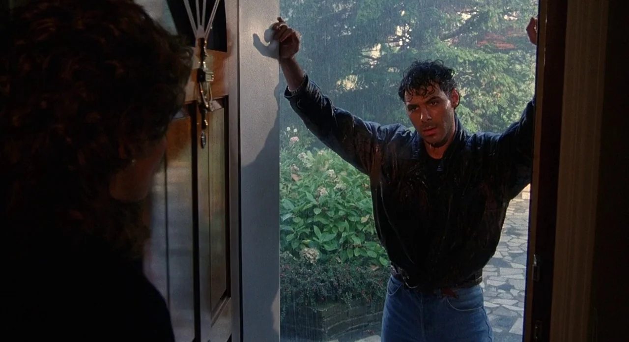 Hellraiser (1987) movie still: medium — A man stands in the doorway during a heavy rain shower. He leans against the door frame looking toward a…
