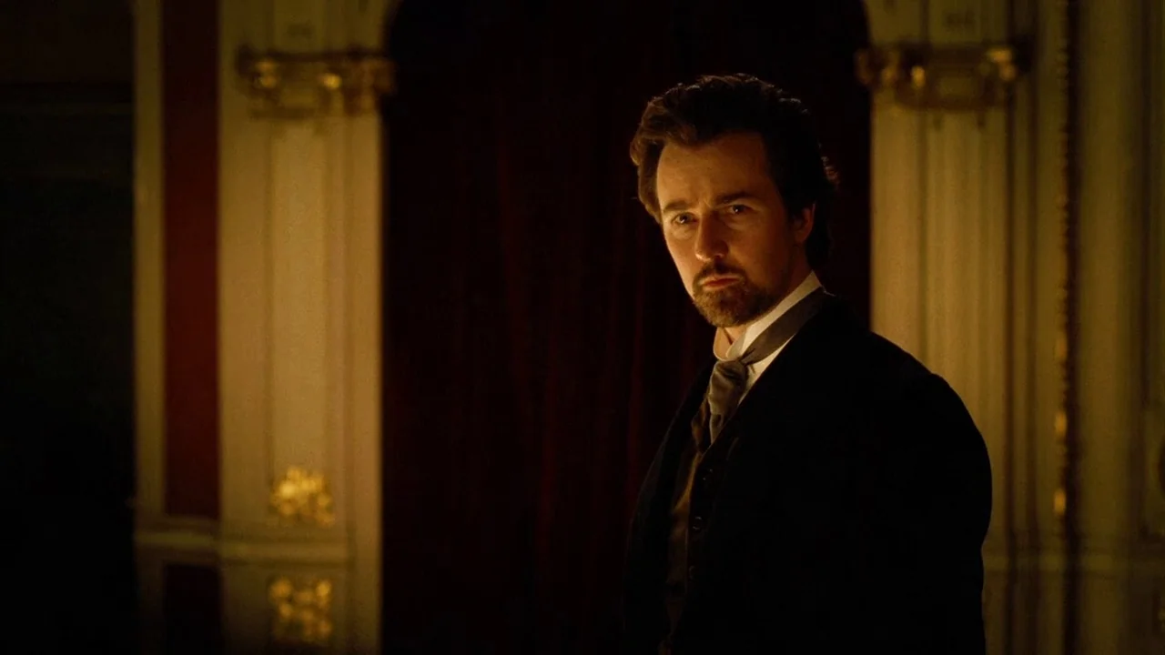 The Illusionist (2006) movie still: medium — A dimly lit room features ornate wood paneling and deep red curtains in the background. A man stands in…