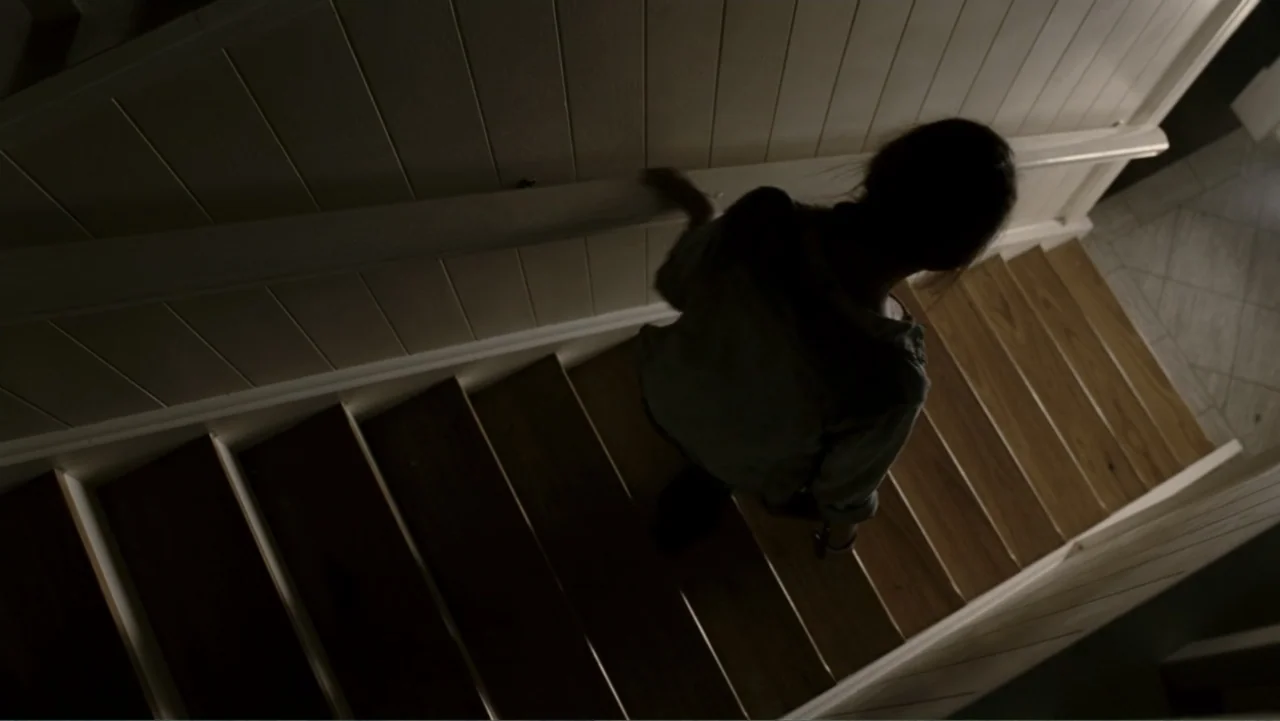 Tomorrow, When the War Began (2010) movie still: medium — A residential interior features a wooden staircase with white vertical plank walls. A…