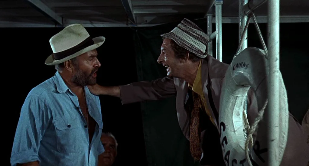 Age of Consent (1969) movie still: medium — Two men stand on the deck of a boat at night against a black background. One man leans in toward the…