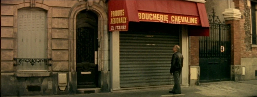 I Stand Alone (Seul Contre Tous) (1998) movie still: wide — A French storefront with a red awning and a closed metal shutter facade. An elderly man…