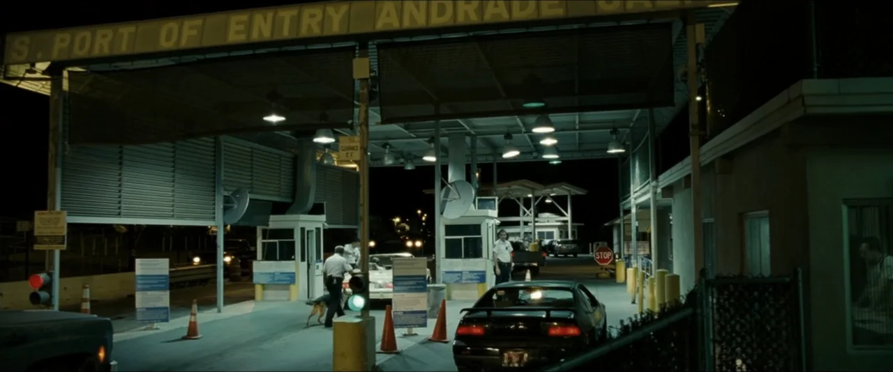 Into the Wild (2007) movie still: wide — A dark, industrial border checkpoint with multiple lanes, overhead metal canopy, and fluorescent lighting.…
