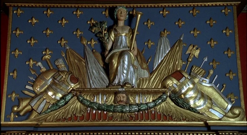 Bluebeard (2009) movie still: closeup — A decorative wall relief displays a central sculpted figure flanked by military imagery. Fleur-de-lis…