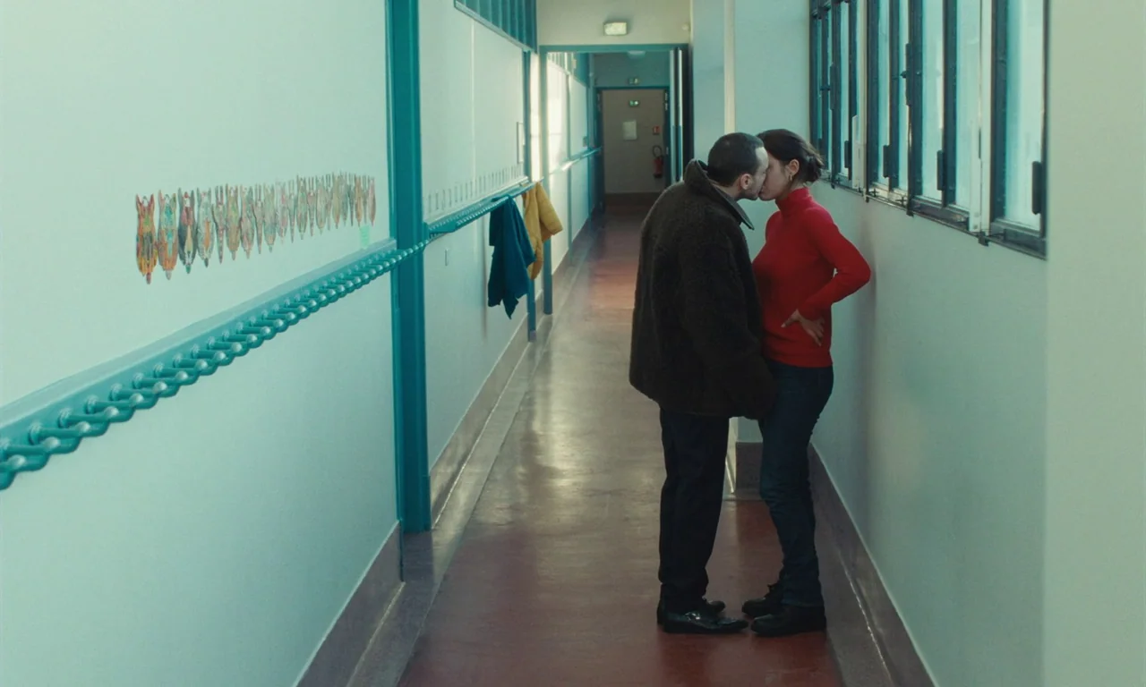 Passages (2023) movie still: fullbody — A long school corridor with turquoise walls features a series of windows and student artwork. A man in a…