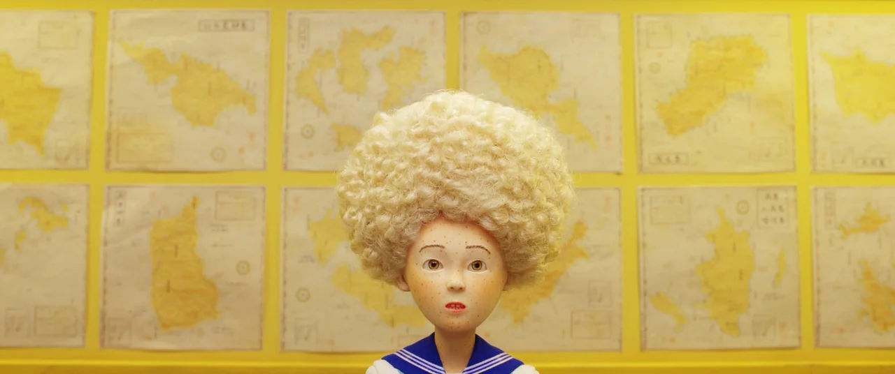 Isle of Dogs (2018) movie still: medium — A yellow-walled classroom features rows of framed maps hanging behind a central character. A young girl…