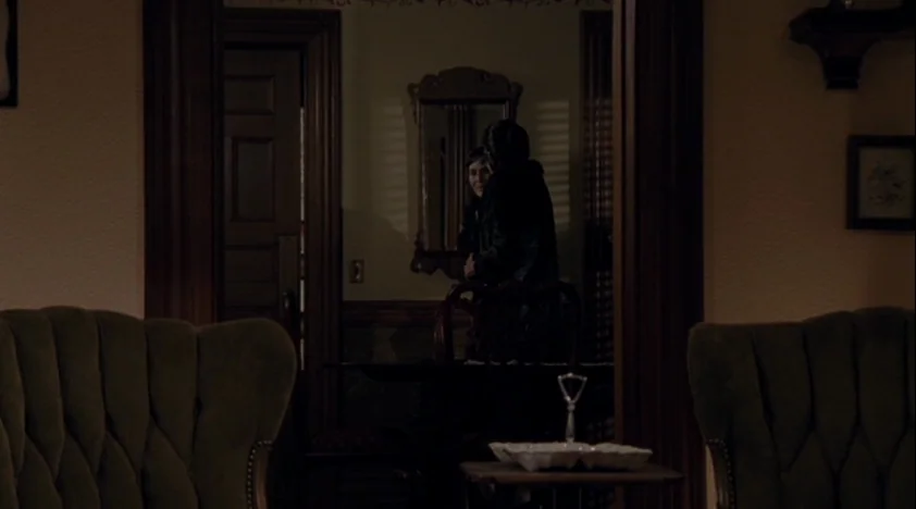 The House Of The Devil (2009) movie still: medium — A dark, dimly lit domestic interior features vintage patterned armchairs in the immediate…