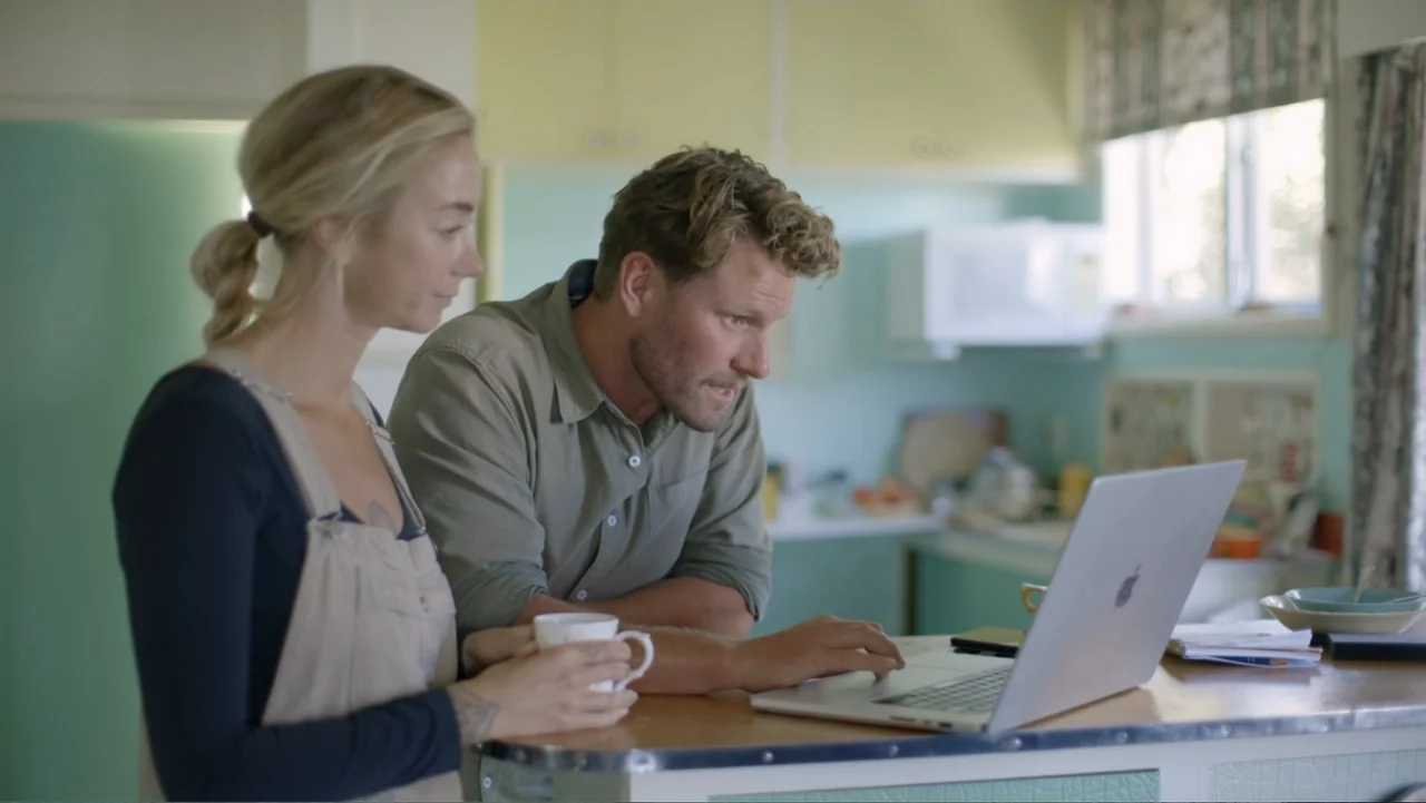 Jaws in the Shallows (2023) movie still: medium — A light-colored kitchen with retro-style mint green cabinets and a breakfast bar. A man and a…