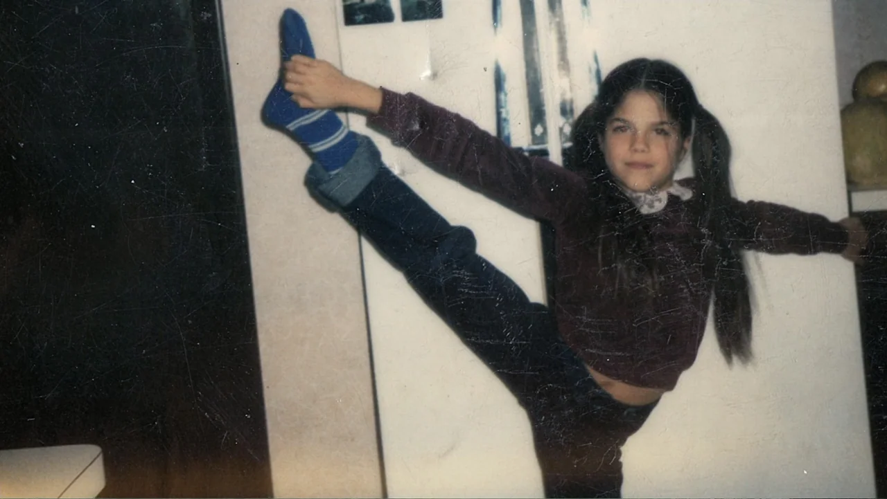 Introducing, Selma Blair (2021) movie still: fullbody — A plain interior room with a white wall serves as a backdrop. A young girl poses with one…