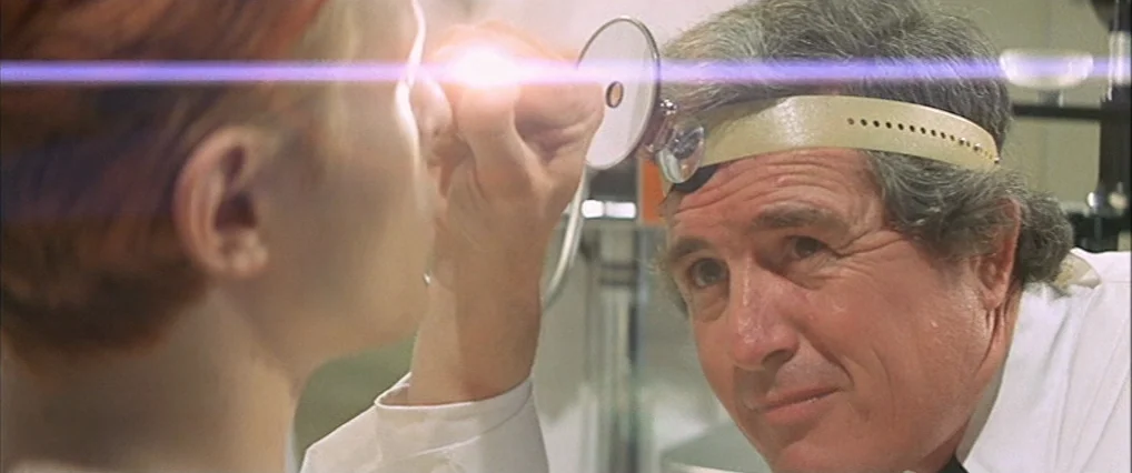 The Man Who Fell To Earth (1976) movie still: medium — A clinical examination room with white walls and professional medical equipment present. A…