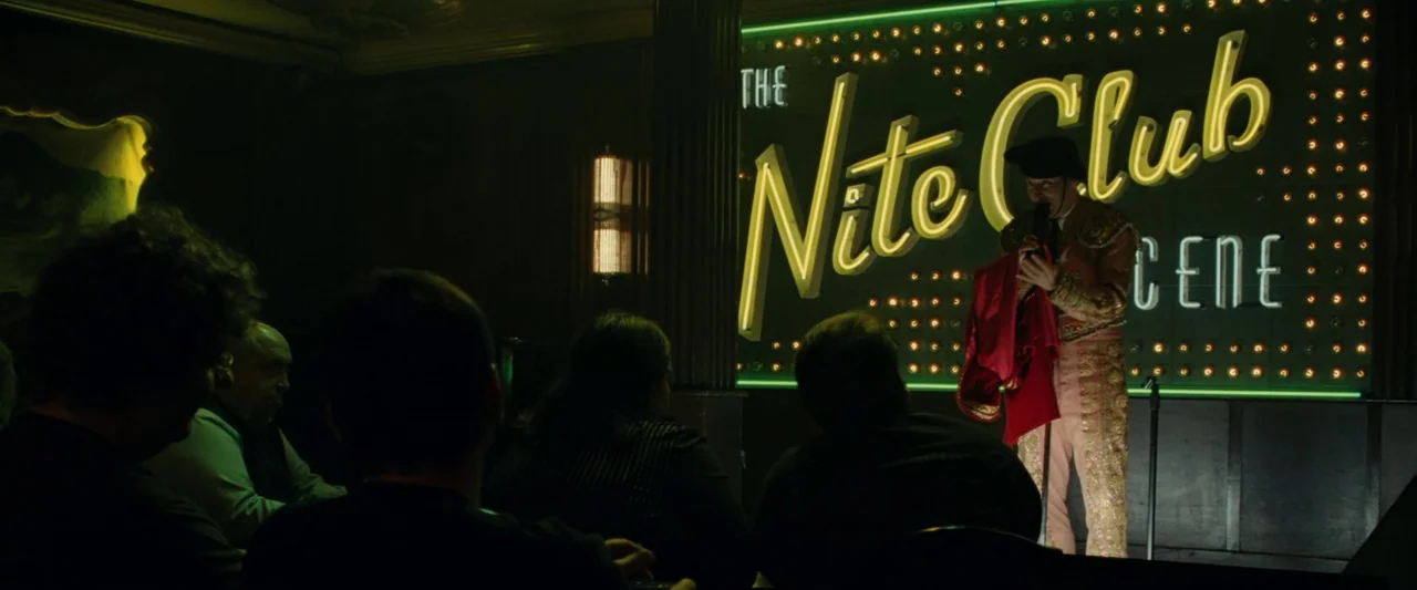 Ocean’s Twelve (2004) movie still: wide — A dimly lit club interior with an audience watching a performer on a stage. A man dressed as a matador…