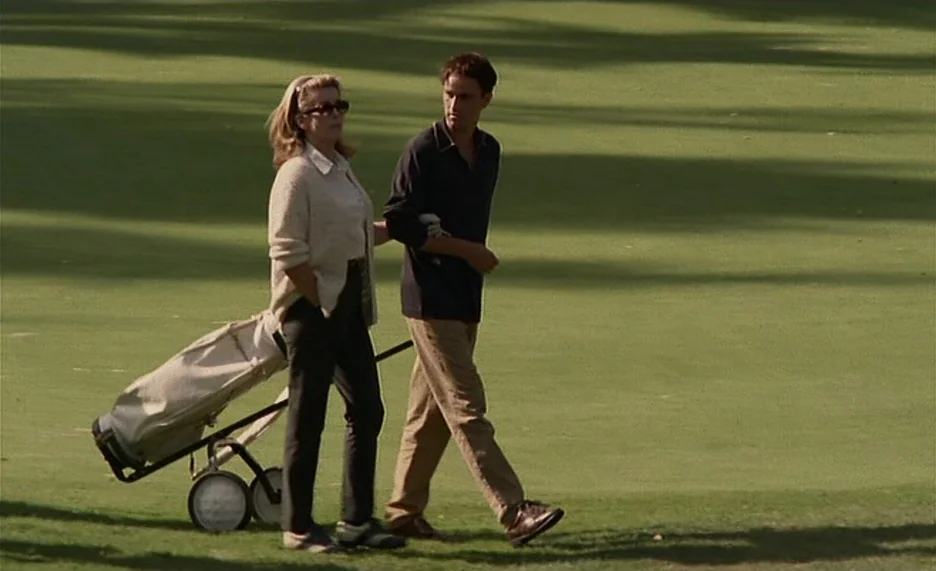 Pola X (1999) movie still: fullbody — An open expanse of green grass on a golf course under natural daylight. A woman and a man walk side by side…